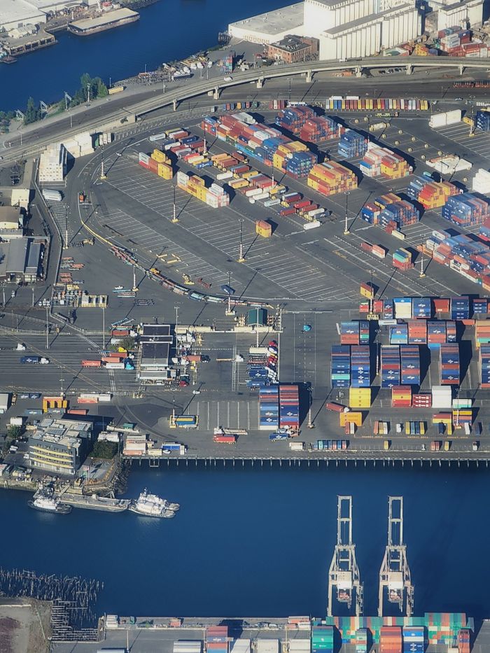 gallery-4 Overhead view of a bustling port with colorful shipping containers and waterfront area.