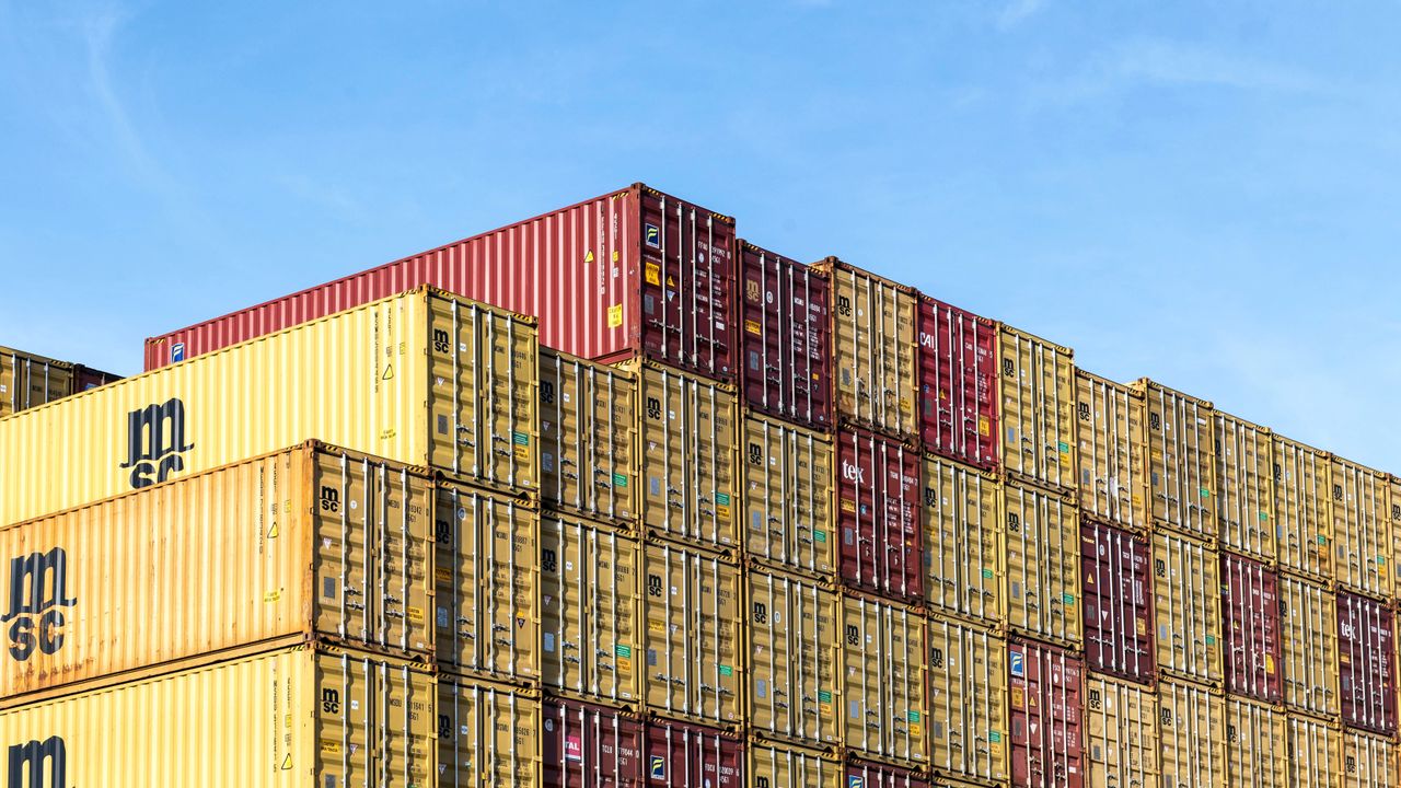 services-03 Colorful stacked cargo containers in Hamburg port under a clear blue sky.