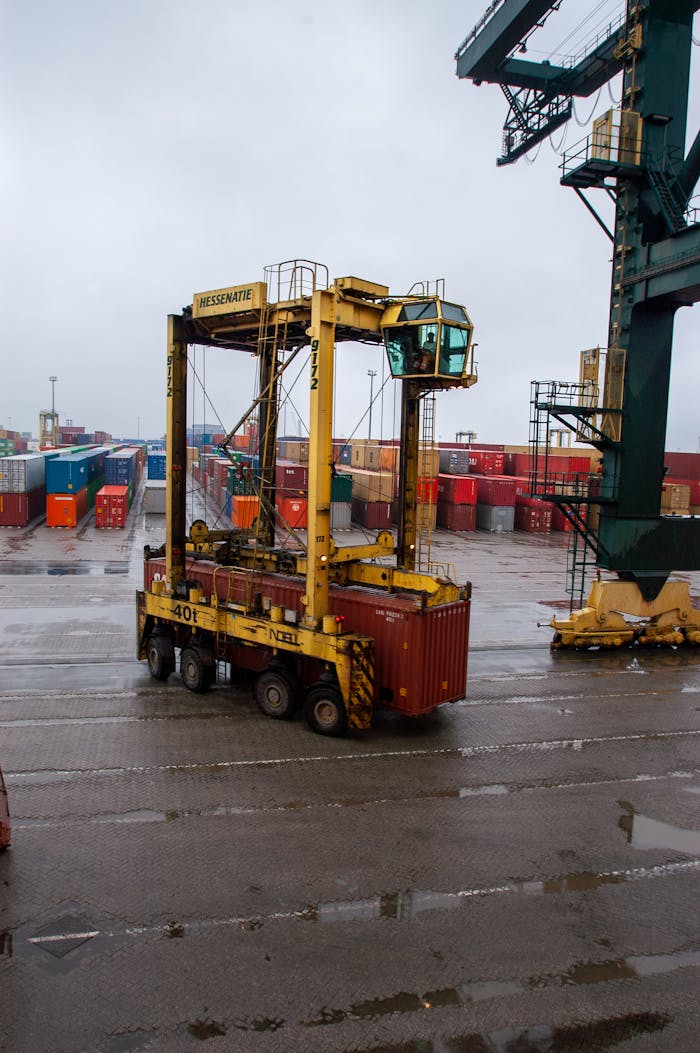 gallery-6 Yellow straddle carrier moving containers at a busy, rainy shipping port.
